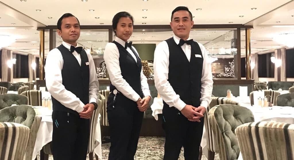 Three restaurant service crew members in an onboard dining room